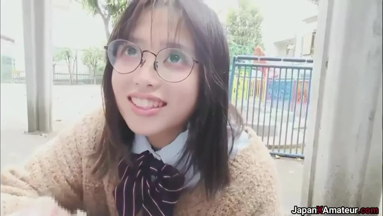 Fille japonaise amateur avec des lunettes faisant une pipe à l'extérieur dans un parc