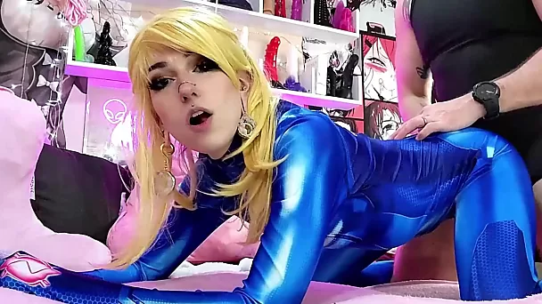 Une ado blonde mince et flexible dans un costume de sexe en latex bleu se fait baiser dans la salle de jeux pour adultes