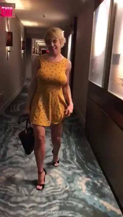Une blonde aux gros seins enlève sa robe dans le couloir de l'hôtel