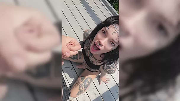 Une transsexuelle tatouée avec une langue fourchue fait une fellation en public au milieu de la forêt.