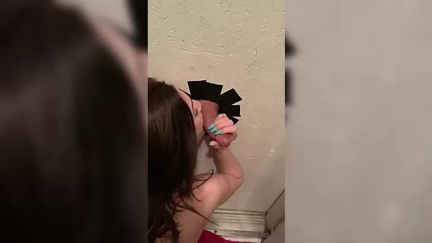 Une brune mince s'occupe de la bite du voisin à travers un glory hole pendant que son mari la regarde