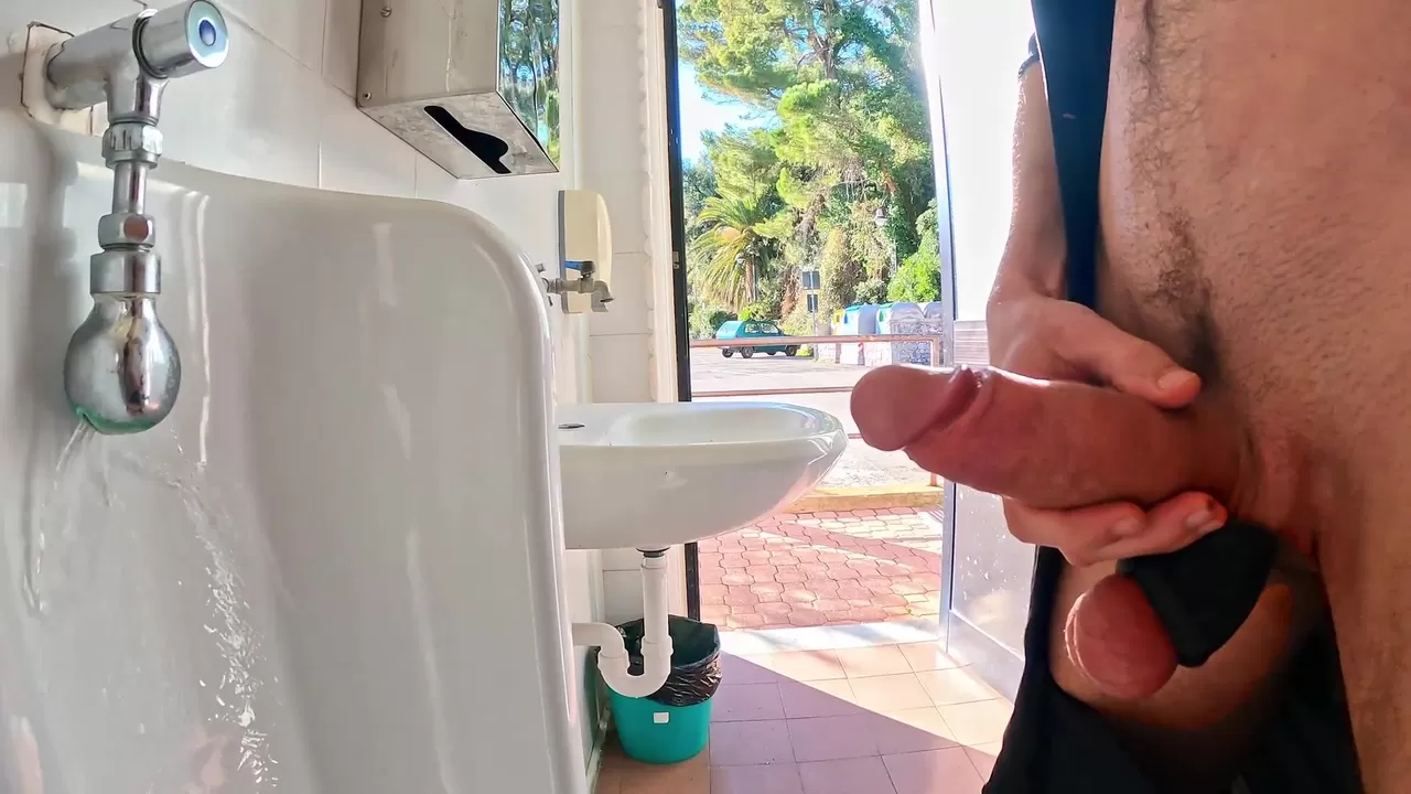 Une bite dure qui pisse dans des toilettes publiques avec la porte ouverte